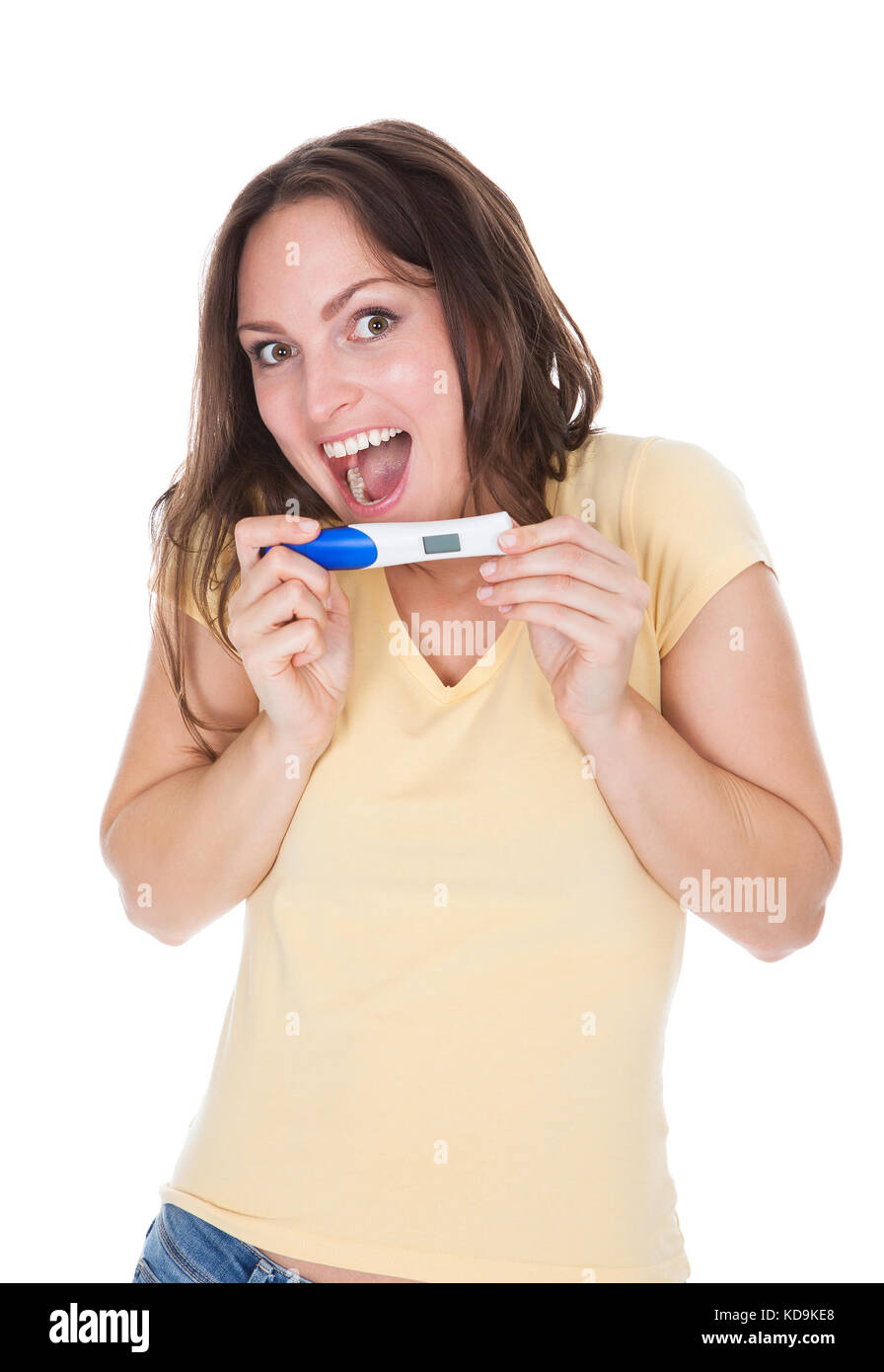 Porträt von Happy Woman Looking At Schwangerschaft Ergebnis Over White Background Stockfoto