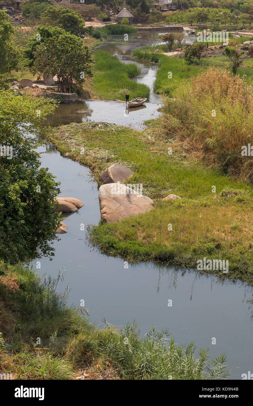 Fließende Fluss mit Felsen, Vegetation, Fischer und Boot in Afrika. lubango. Angola. Stockfoto