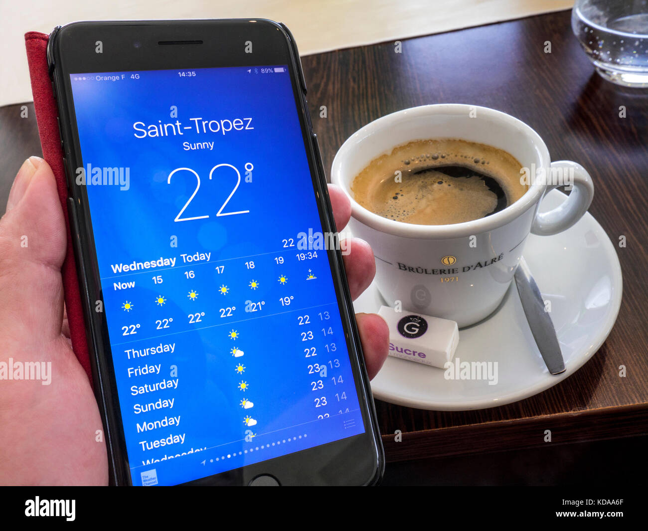 WETTER-APP SAINT TROPEZ im Restauranttisch Situation Espresso-Kaffeetasse dahinter, Bildschirm mit einer typisch sonnigen, warmen Wettervorhersage für Saint-Tropez Cote d’Azur Frankreich für 22C Stockfoto