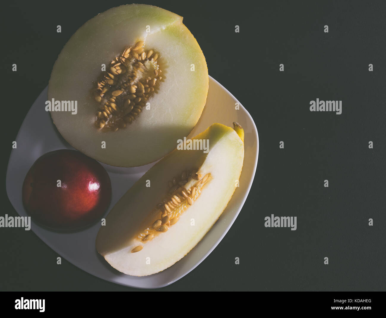 Weiß melone Melone mit einem roten Pfirsich auf einem weißen Teller. dunklen Hintergrund. Stockfoto