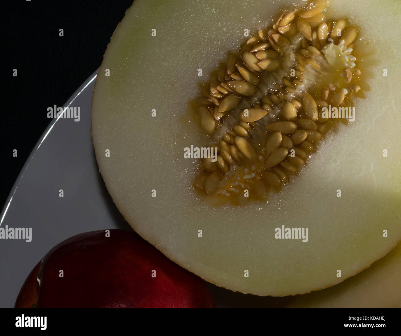 Weiß melone Melone mit einem roten Pfirsich auf einem weißen Teller. dunklen Hintergrund. Nach oben Schließen Stockfoto