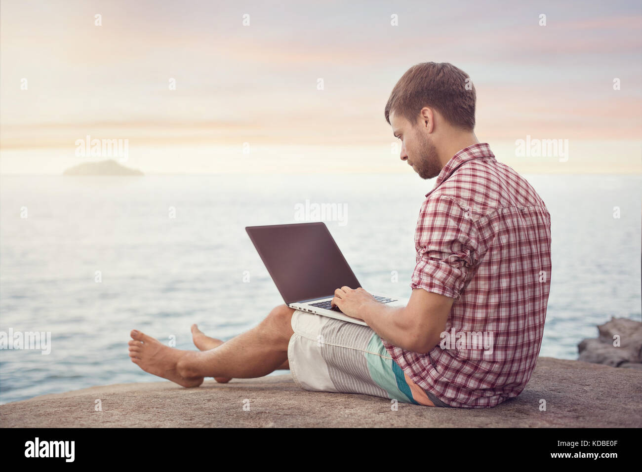 Mann mit Laptop sitzen neben dem Ocean Stockfoto