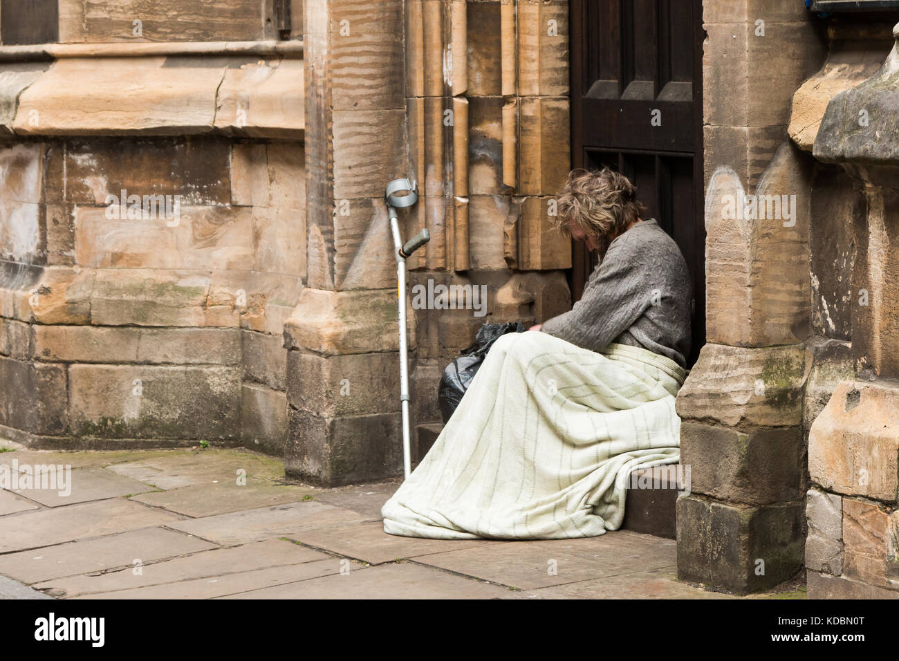 Obdachloser in York Großbritannien ruht. Decke über seine Knie, Arm Krücke, lehnte sich gegen die Wand. Der Mann lokking sehr traurig, verloren und einsam. graues Haar Stockfoto