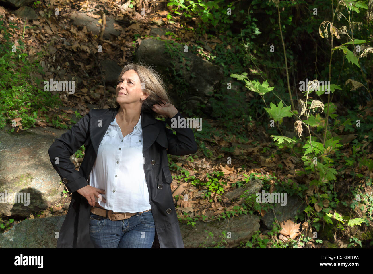 Ältere Frau, 61 Jahre alt, trug einen Trenchcoat und Jean, Herbst, Natur Hintergrund. Stockfoto
