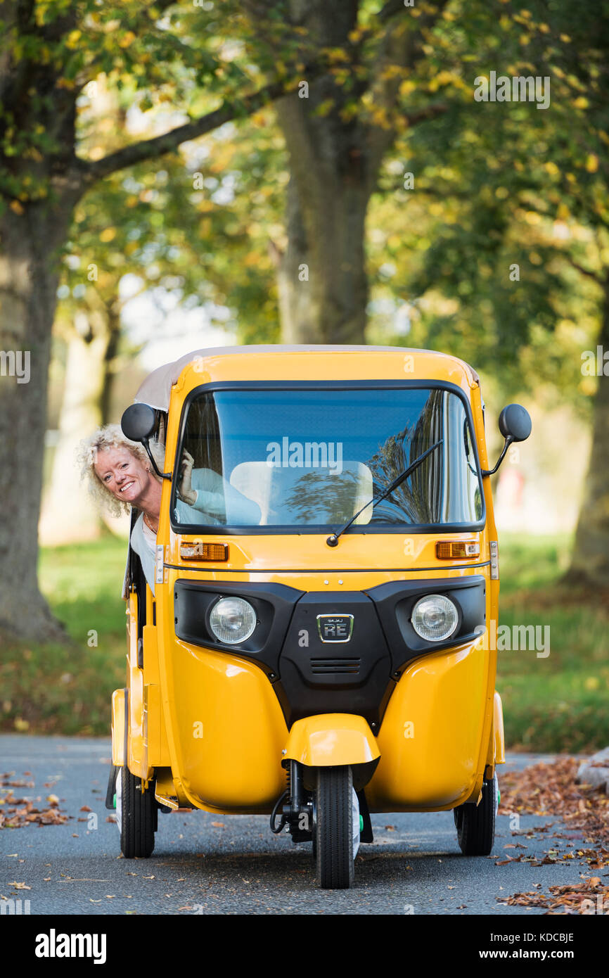 Eine blonde Frau fährt einen gelben Tuk Tuk in einem englischen Dorf Stockfoto