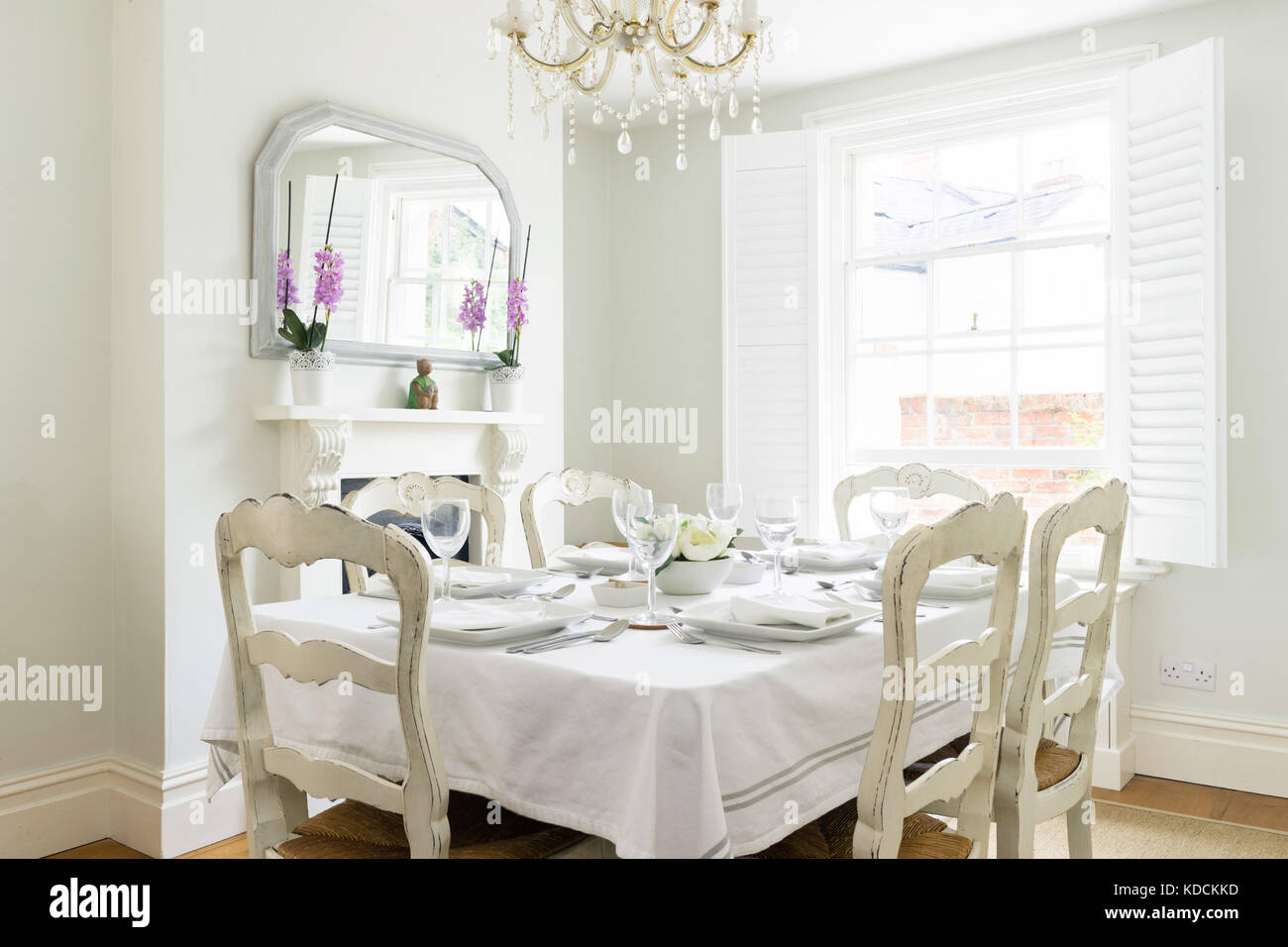 Ein helles, Vintage gestalteten Speisesaal in einem viktorianischen Haus, in dem ein gedeckter Tisch mit Stühlen, geschlossene Fenster, Kronleuchter und einen Kamin. Stockfoto