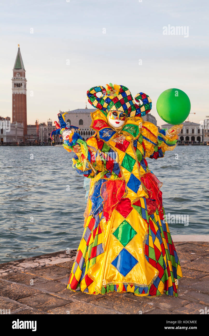 2017 Karneval in Venedig, Venedig, Italien. Bunte Harlekin Frau Jester bei Sonnenuntergang mit der Lagune und Campanile hinter ihr Posing Stockfoto