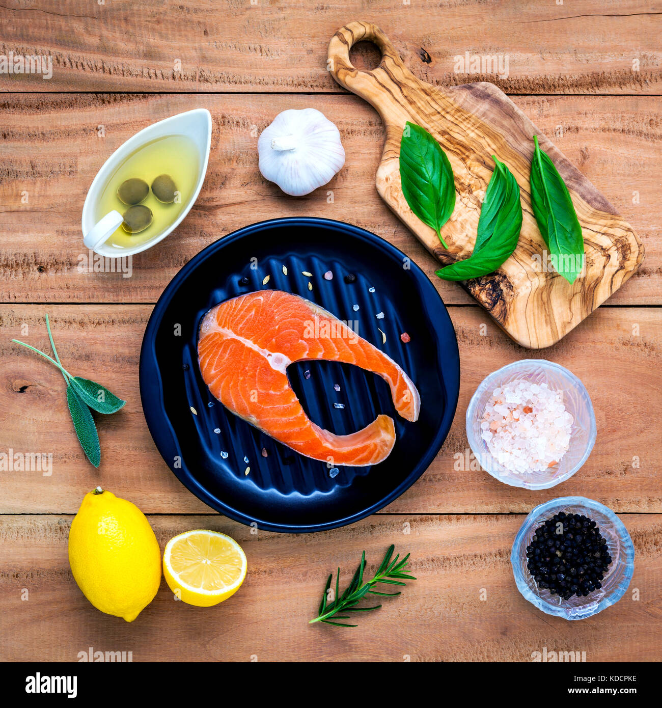 Rohes Lachsfilet in die schwarze Platte mit Zutaten Olivenöl, Himalaya Salz, Kräuter, Basilikum, Fenchel, Salbei, Rosmarin, Knoblauch, Pfeffer und Lem Stockfoto