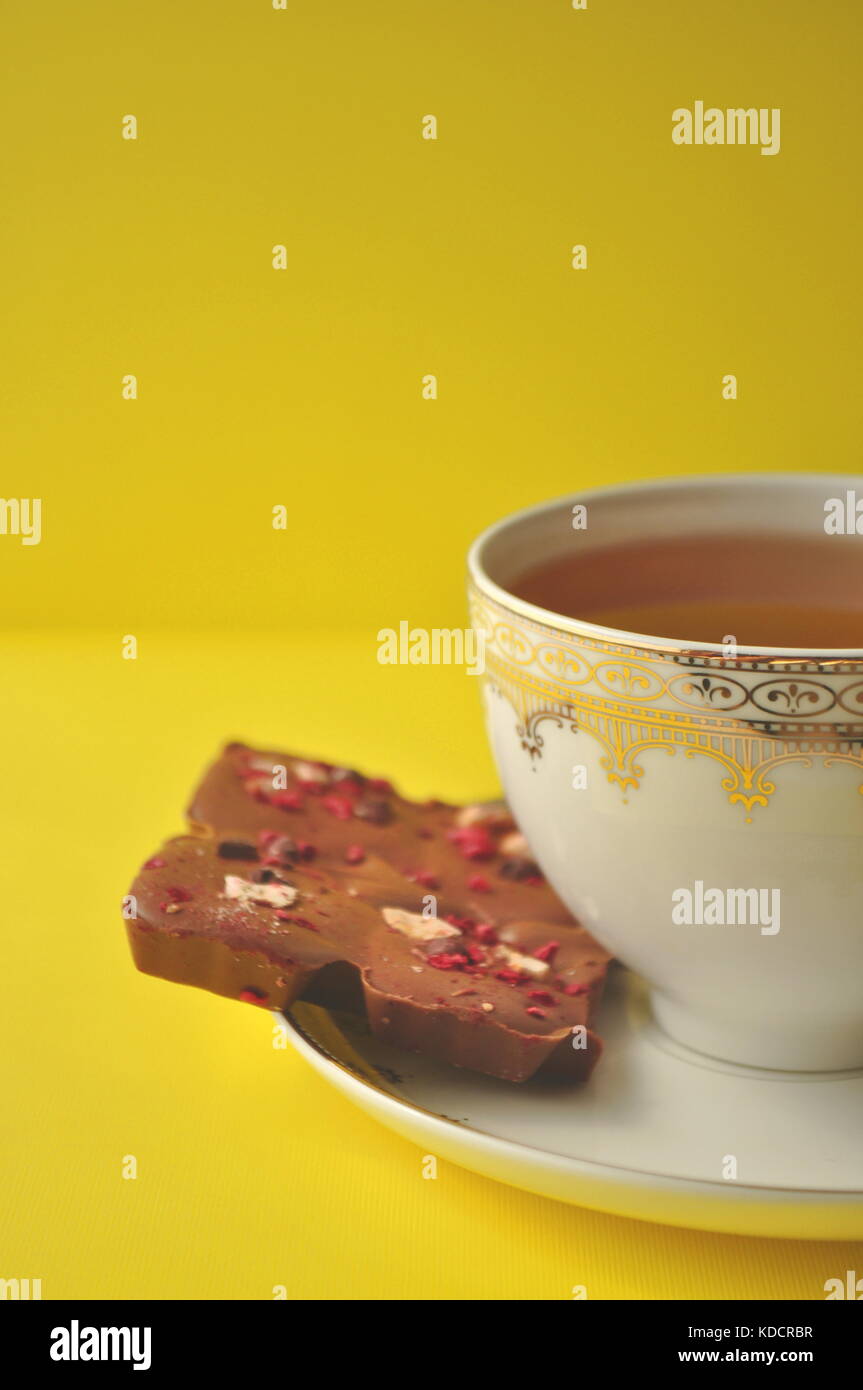 Heißen Tee in einer Porzellan Tasse mit Artisan Schokolade, ein offenes Buch auf einem leuchtend gelben Hintergrund mit kopieren. Freizeitaktivitäten, Lesen und Entspannen. Stockfoto