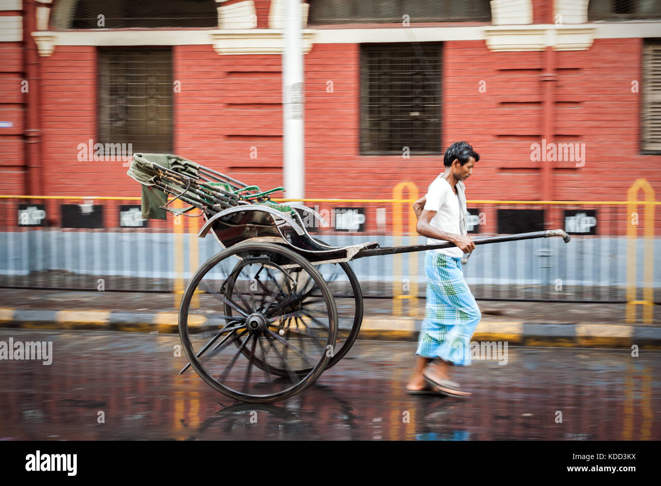 Manuelle Rikscha wala auf den nassen Straßen von Kolkata in Indien. Einer der wenigen Plätze dieser Besetzung zu sehen. laufender Mann ziehen Rikscha auf der Straße Stockfoto
