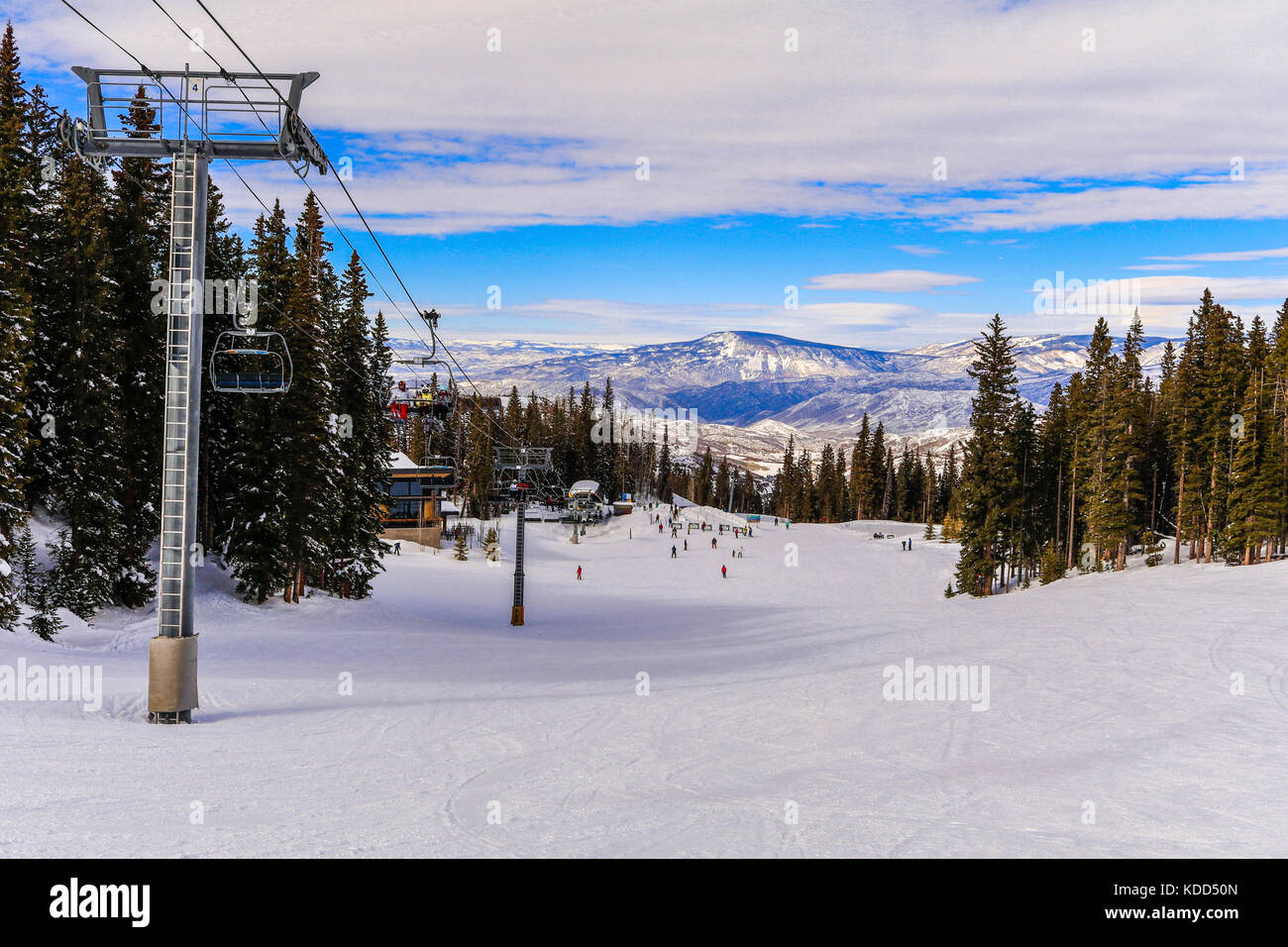 Ansicht eines Snowmass, Colorado am Nachmittag; Skifahrer und Snowboarder ski den Hang hinunter auf der Basis einer Sesselbahn; Berge im Hintergrund Stockfoto