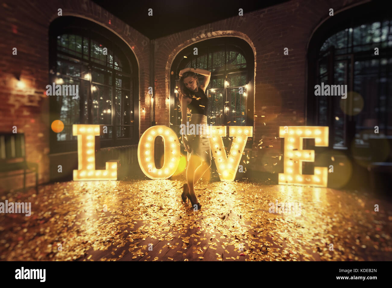 Schöne Mädchen vor dem Hintergrund der glänzenden Buchstaben posieren. Aus den Buchstaben das Wort "Liebe" besteht. goldenen Blütenblätter sind verstreut auf dem Boden. Stockfoto