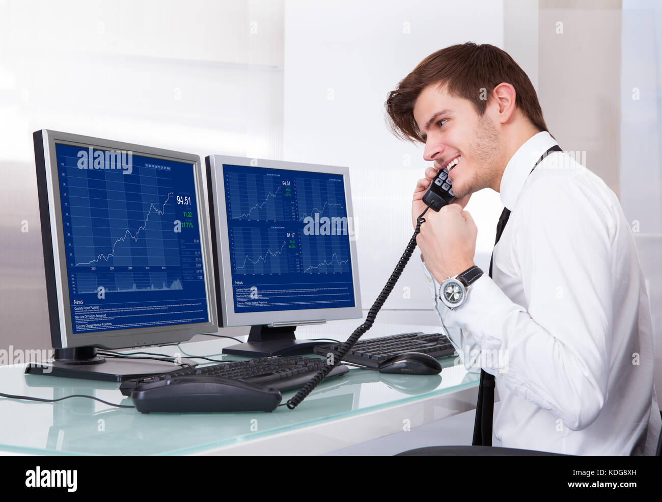 Börsenmakler mit Telefon vor Desktop Sitzung Stockfoto