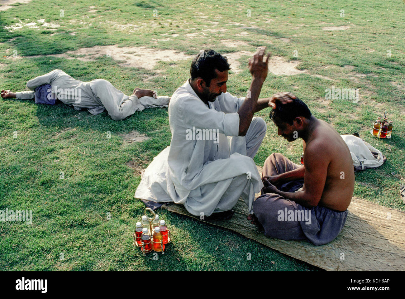 Ein Kopf Masseur bietet eine Massage auf dem Gelände des Shah Rukn-i-Alam Schrein, Multan, Pakistan. Stockfoto