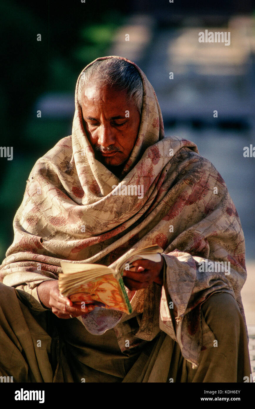 Ein Mann, der in einen Schal gewickelt ist, liest ein Buch mit einem bunten Cover. Stockfoto