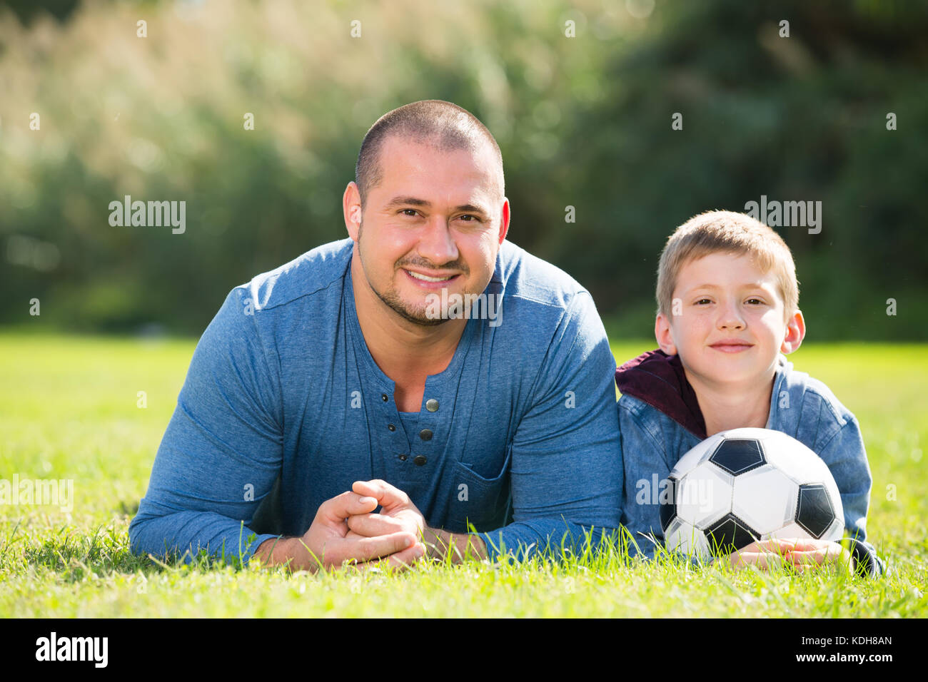 Freundlich lächelnden Teenager Sohn und Vater im Gras liegend zusammen mit Fußball-Ball. Im Mittelpunkt der Mensch Stockfoto