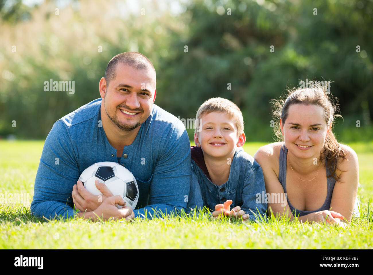 Mutter, Vater und glückliche Junge im Gras mit Fußball liegen Stockfoto