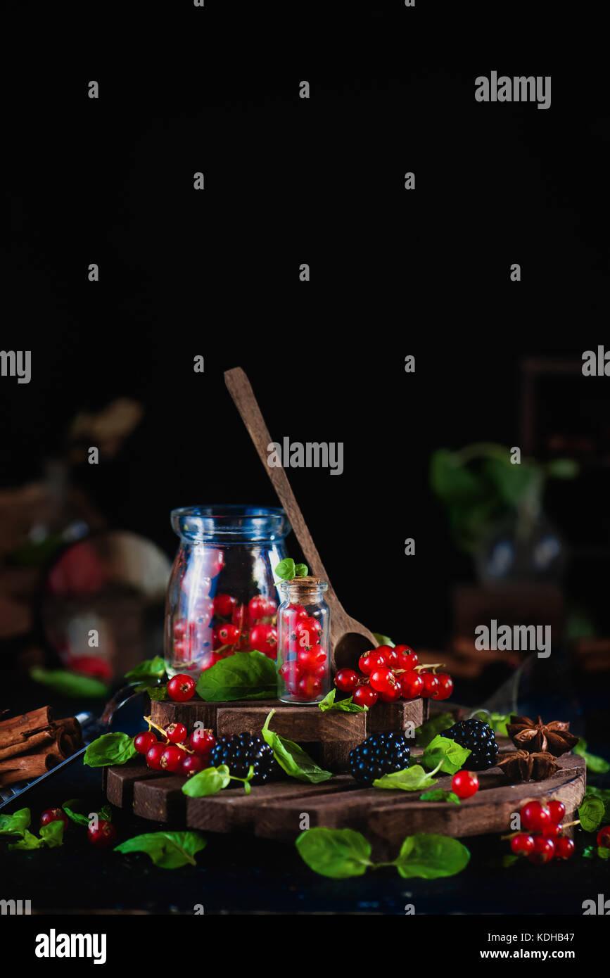 Glas mit frischen Johannisbeeren und Blackberry mit Löffel aus Holz auf einem schwarzen Hintergrund. Labor und Wissenschaft Konzept. magische Stillleben mit Zimt und ein Stockfoto