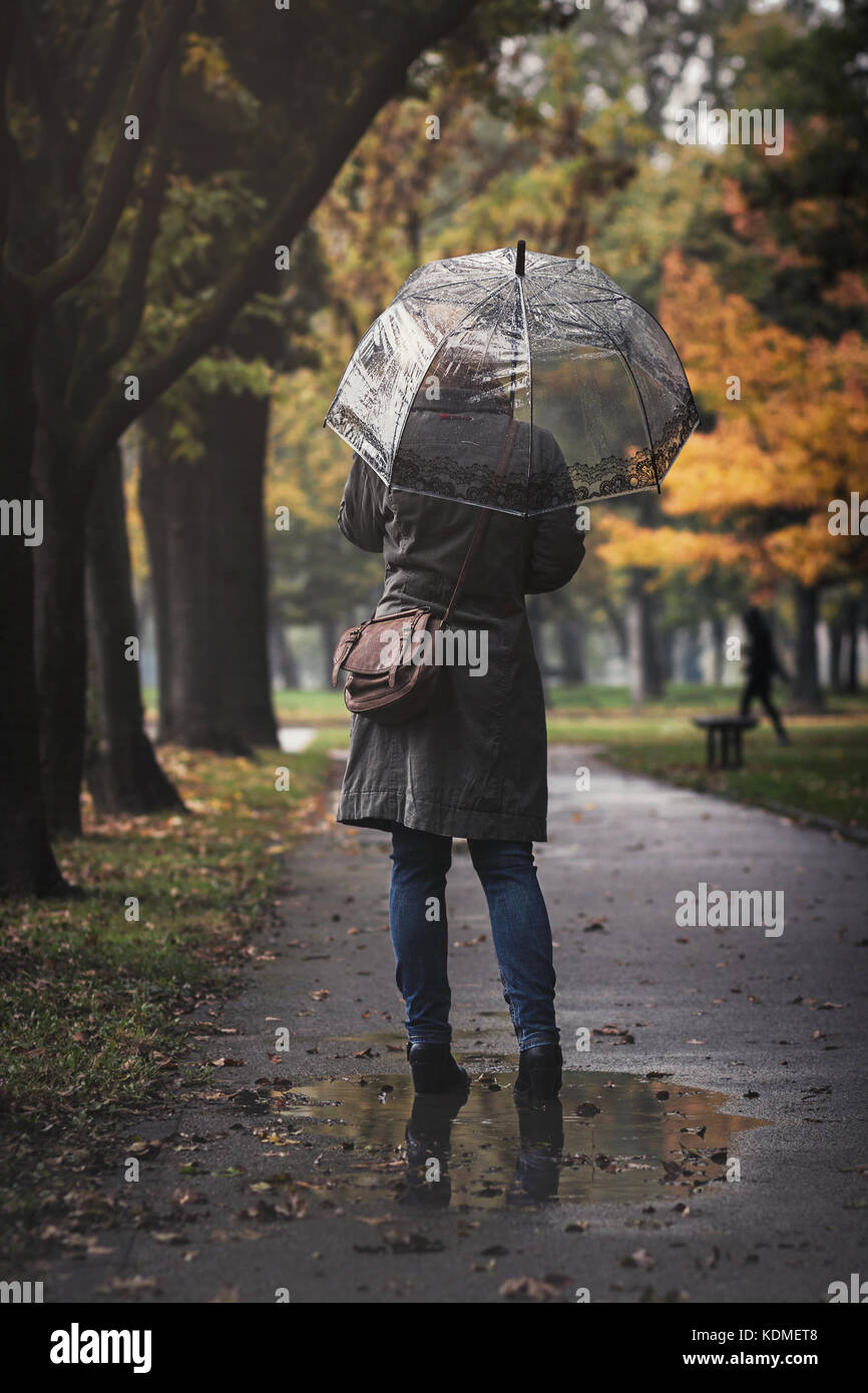 Frau mit transparenten Regenschirm an einem regnerischen Tag in einer Pfütze Stockfoto