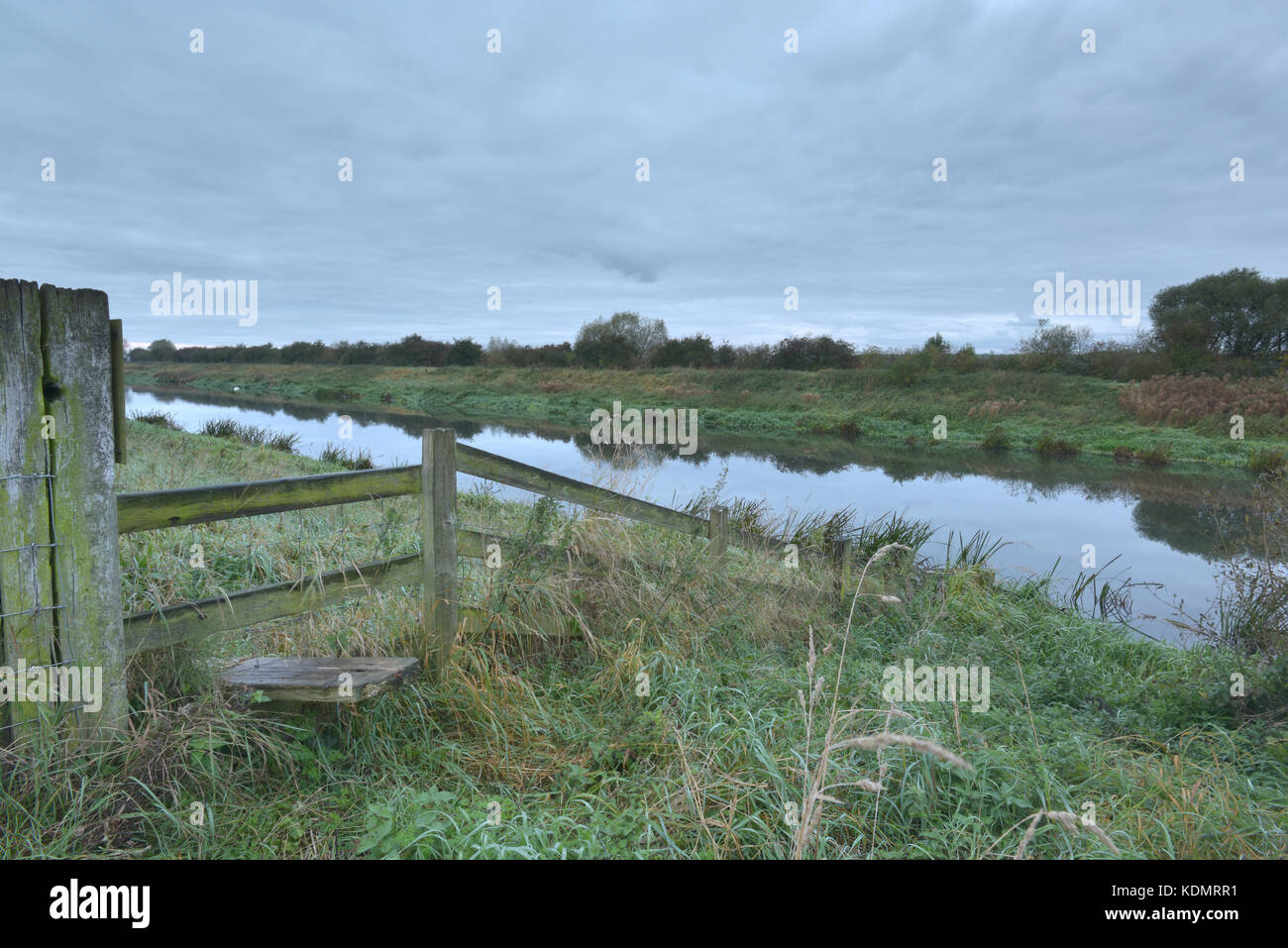 Ein Stil über eine Hecke oder Zaun auf einem öffentlichen Fußweg in der Nähe von dunston auf der Lincolnshire fens oder Moorland mit einem bewölkten Morgen Himmel und reflektiert. Stockfoto