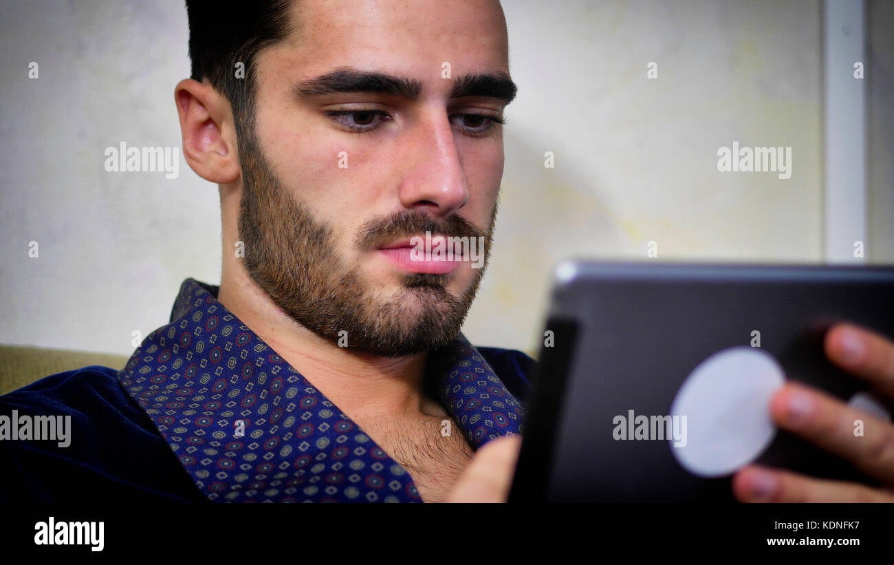 Junger Mann auf der Couch lesen mit Tablet-PC Stockfoto