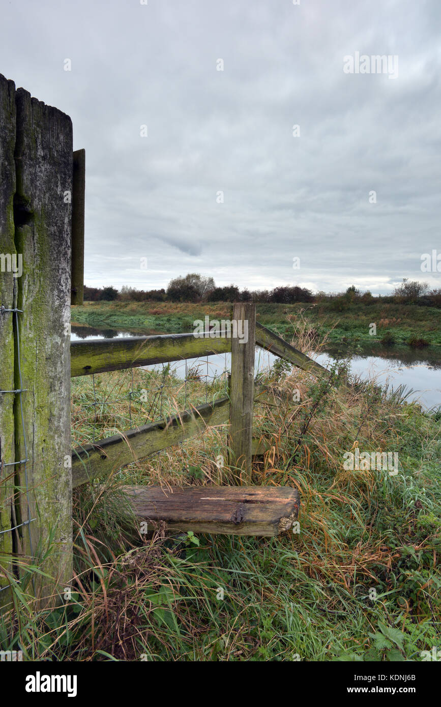 Ein Stil über eine Hecke oder Zaun auf einem öffentlichen Fußweg in der Nähe von dunston auf der Lincolnshire fens oder Moorland mit einem bewölkten Morgen Himmel und reflektiert. Stockfoto