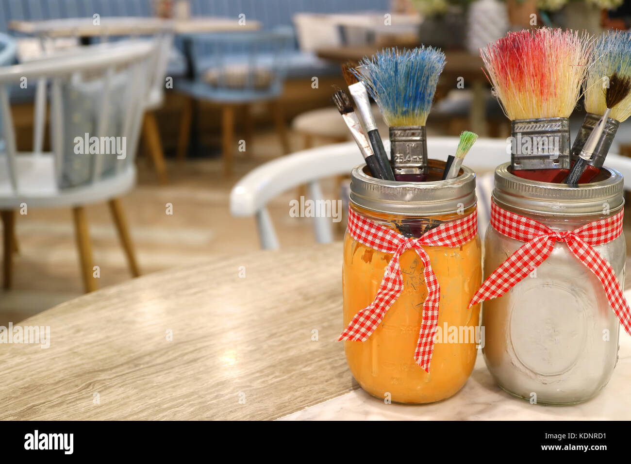 Farbe - Bürsten in der Gläser auf Holztisch mit unscharfen Tische und Stühle im Hintergrund Stockfoto