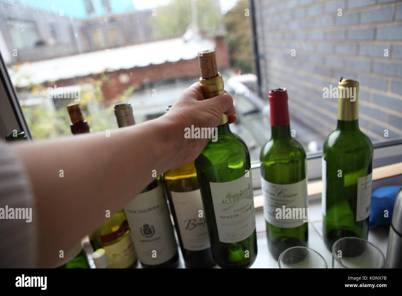 Eine Hand legt eine leere Flasche Wein mit der Reihe der anderen leeren Weinflaschen. Stockfoto