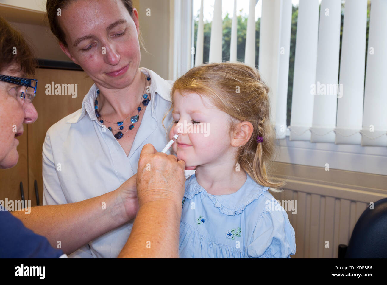 3 Jahre altes Kind, mit ihrer Mama/Mutter, erhält Dosis der Fluenz Grippeimpfstoff Nasenspray Immunisierung von NHS Praxiskrankenschwester UK. (90) Stockfoto