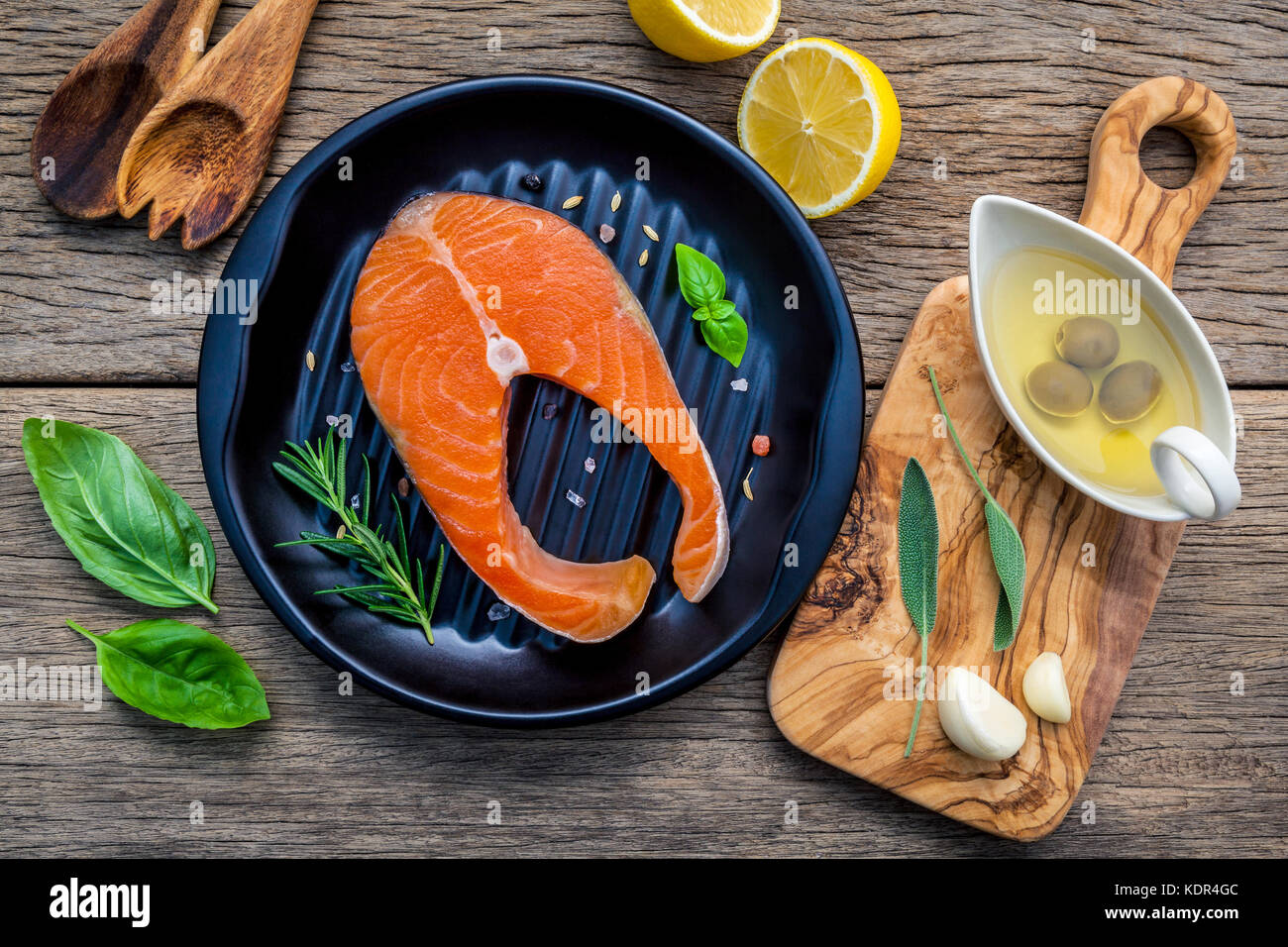 Rohes Lachsfilet in die schwarze Platte mit Zutaten Olivenöl, Himalaya Salz, Kräuter, Basilikum, Fenchel, Salbei, Rosmarin, Knoblauch, Pfeffer und Lem Stockfoto
