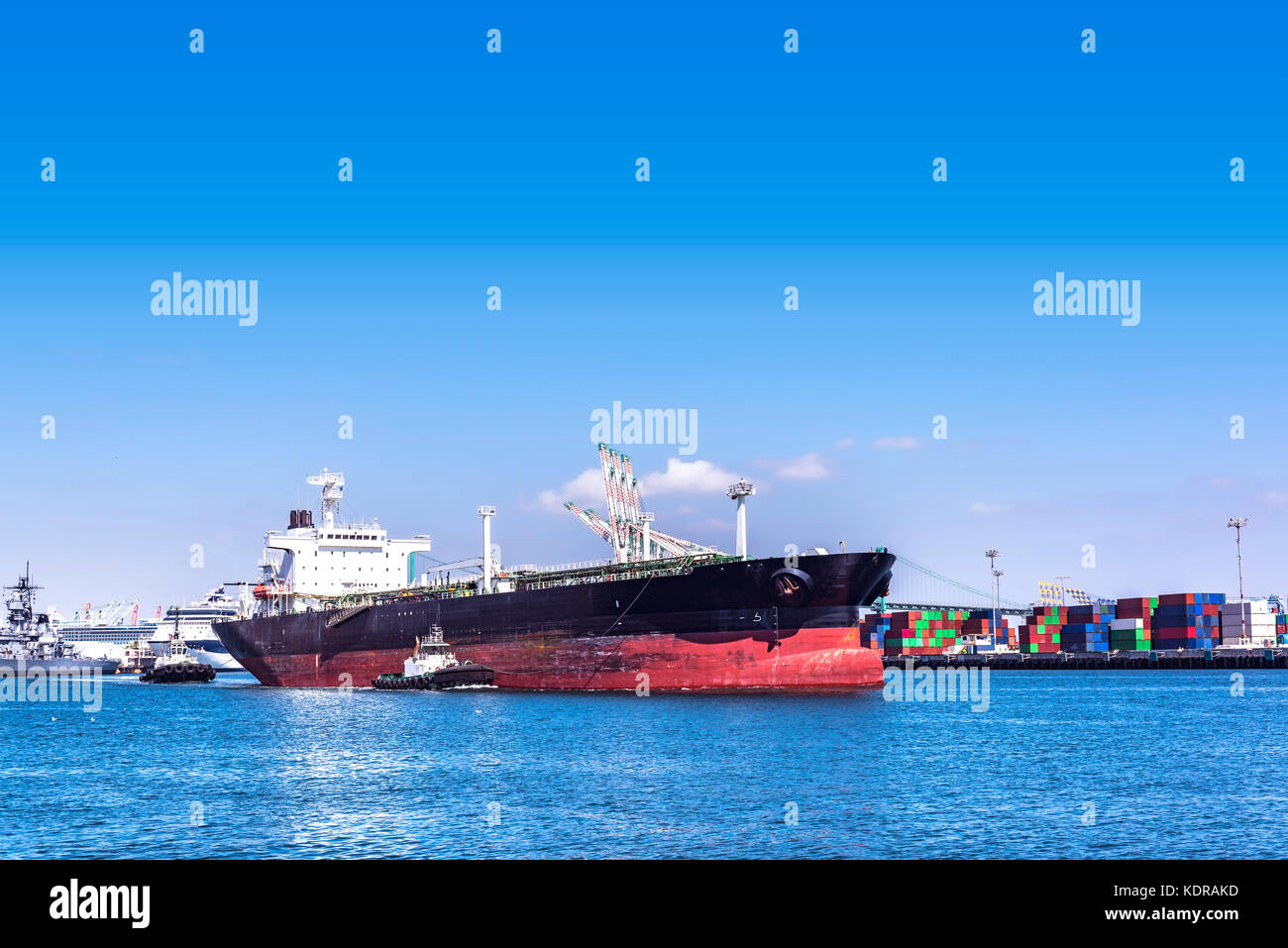 Ein leerer Öltanker wird an einem sonnigen Tag von zwei mächtigen Schleppern aus dem langen Strandhafen befahren Stockfoto