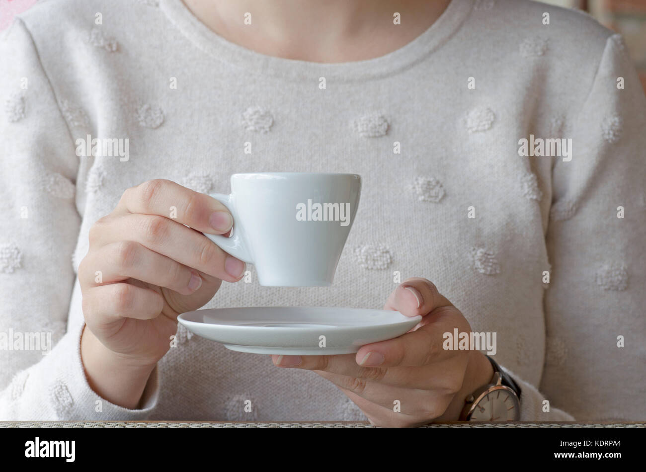 Nahaufnahme einer Frau trinkt Kaffee aus weißem Porzellan Tasse und Untertasse an einem Holztisch Stockfoto