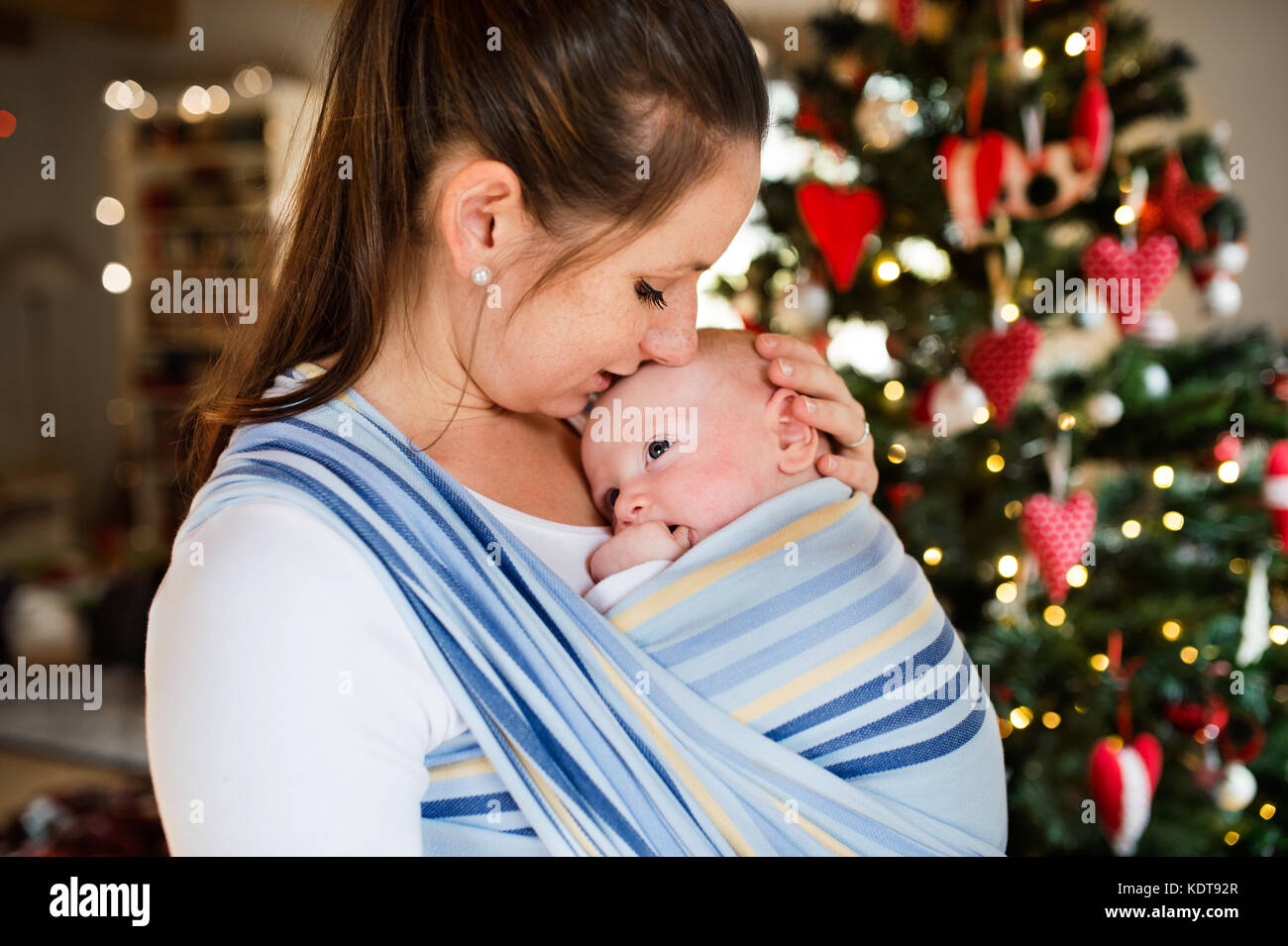 Schöne junge Frau, die ein Baby boy in einem Wrap zur Weihnachtszeit. Stockfoto