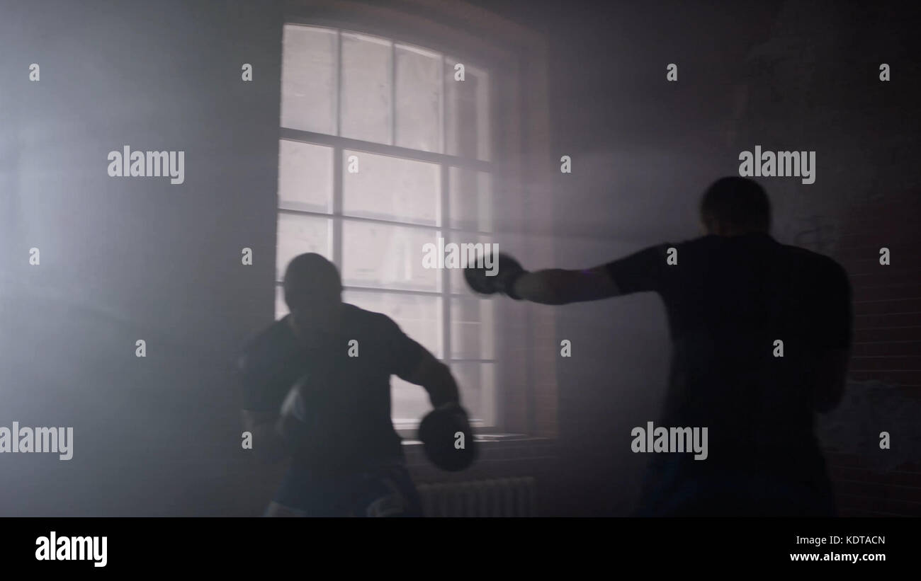 Zwei Boxer trainieren auf dem Ring. Tritt und blockiert den Treffer. Ein Athlet in blauen Boxhandschuhen, der zweite in roter Sportuniform. Die Athleten kämpfen vor dem Hintergrund eines gemauerten Loft Stockfoto