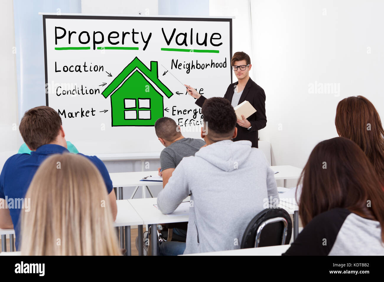Ein männlicher Lehrer, der den Schülern im Klassenzimmer das Konzept des Immobilienwerts erläutert Stockfoto
