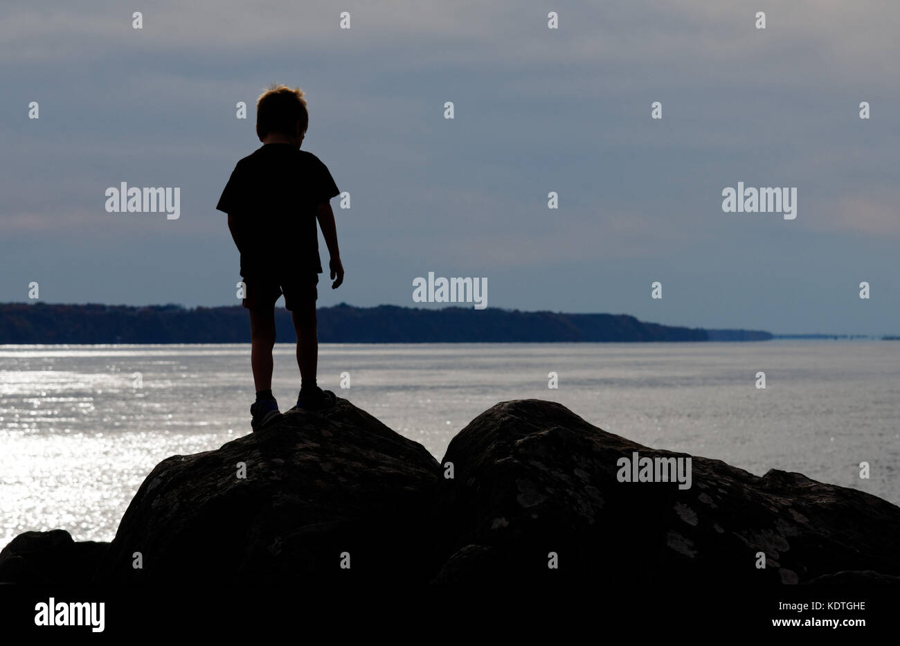 Ein kleiner Junge (5 Jahre alt) silhouetted auf Felsen auf der St. Lawrence River shore bei Cap Rouge in der nähe von Quebec, Kanada Stockfoto
