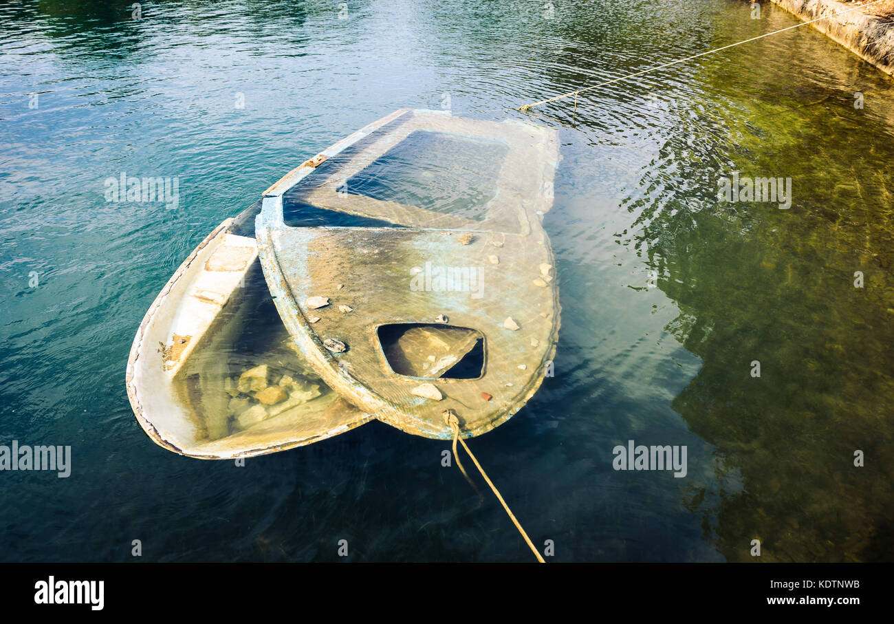 Versunkene Holz- Boot im Meer oder See gebunden. kleine Plastik Boot mit gebrochenen Top eingetaucht ist int er Meer während noch zum Ufer und Pier mit Ro gebunden Stockfoto