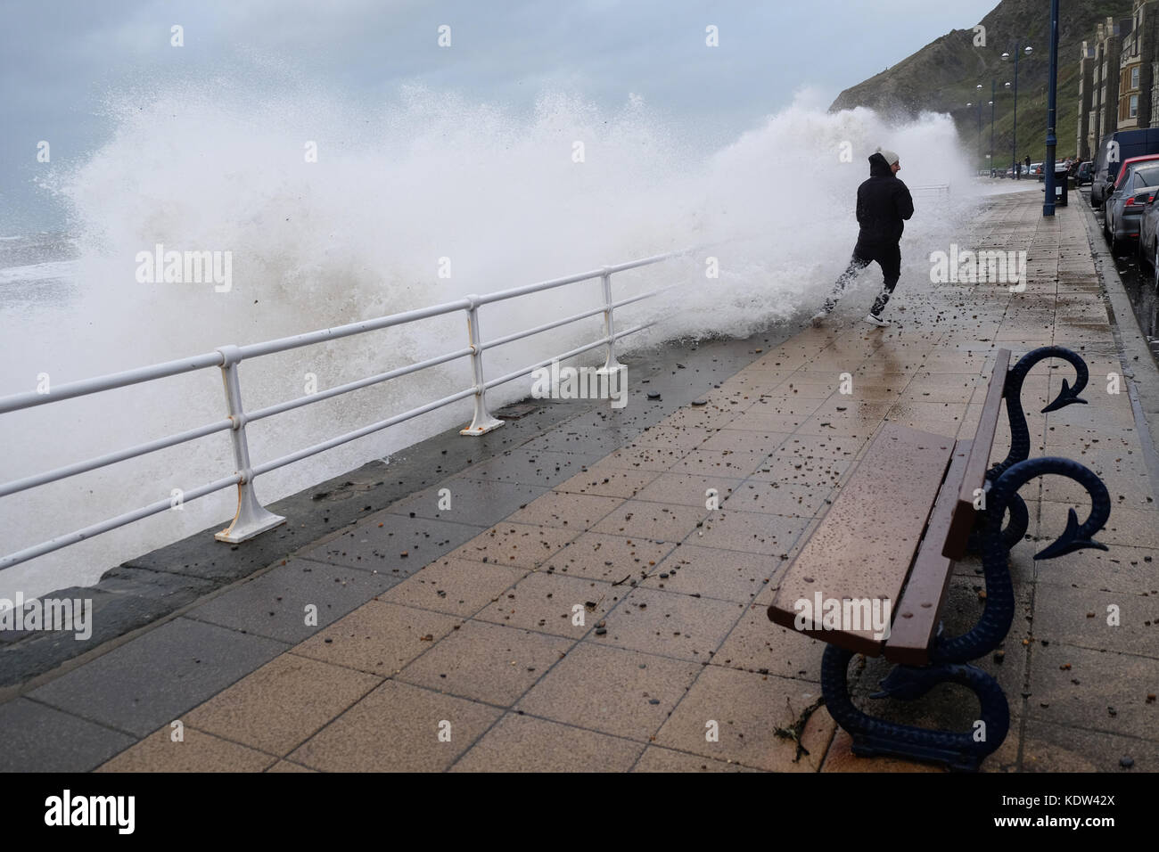 Aberystwyth, Ceredigion, Wales, UK-Flut kommt mit Sturm Ophelia offshore über die Irische See - ein Mann erhält durchnäßt, als der Sturm das Meer Wimpern - Peebles und Kies fliegen auf der Promenade-stong Winde in Aberystwyth auf der West Wales Küste als Sturm Ophelia Ansätze aus der Irischen See mit lokalen Winden von mehr als 50 km/h. Foto Steven Mai/Alamy leben Nachrichten Stockfoto