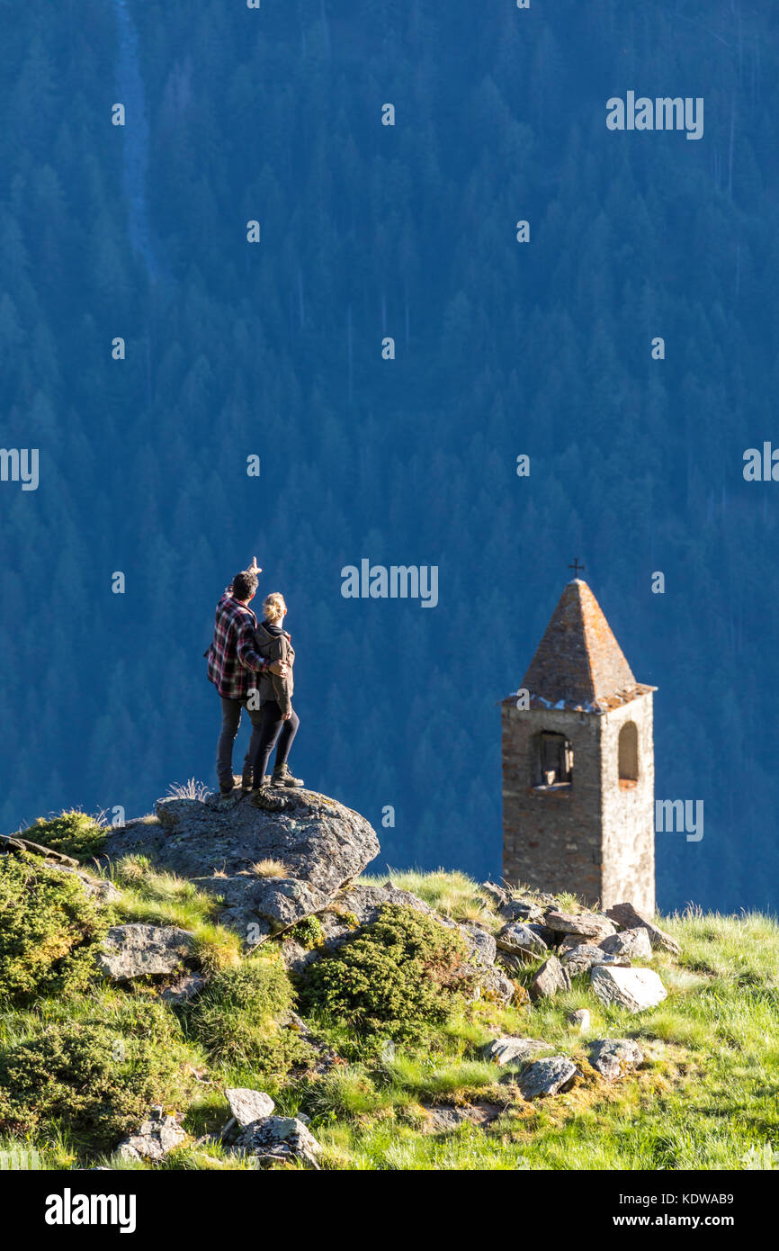 Mann und Frau umarmten Blick auf den Glockenturm, Alp San Romerio, Brusio, Kanton Graubünden, Poschiavo Tal, Schweiz Stockfoto