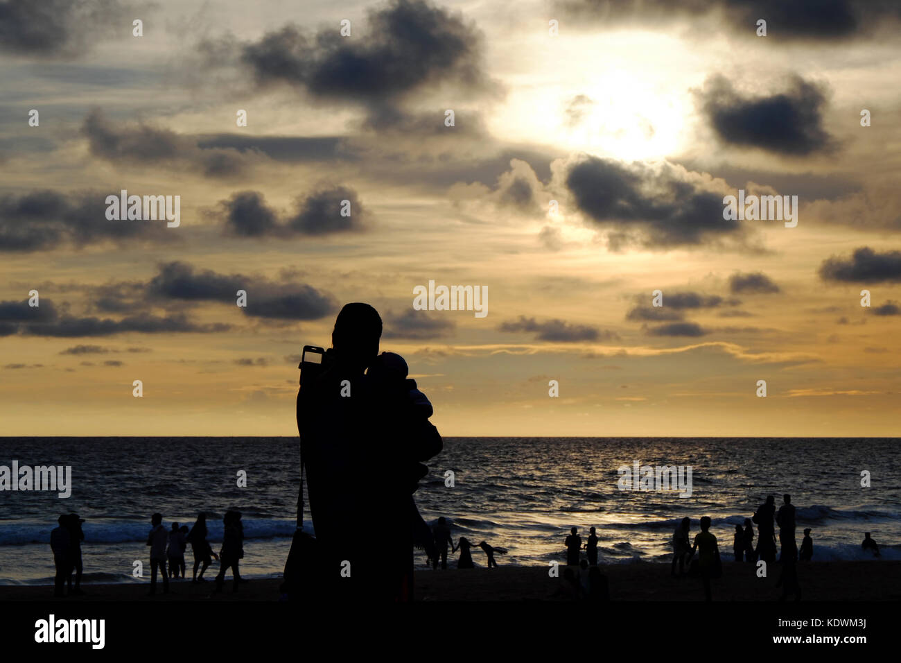 Silhouetten von Frau mit Kind und Menschen, die einen wunderschönen Sonnenuntergang am Strand des Indischen Ozeans beobachten Stockfoto