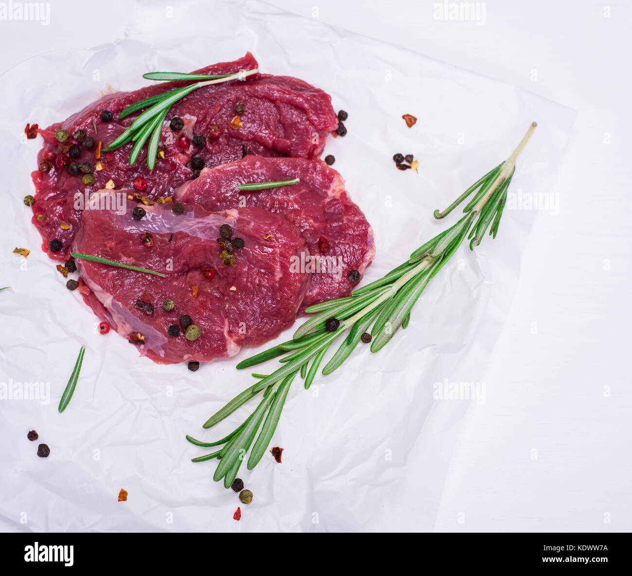 Rohes Rindfleisch Steaks mit Gewürzen und Rosmarin auf weißem Papier, leeren Raum auf der rechten Seite Stockfoto