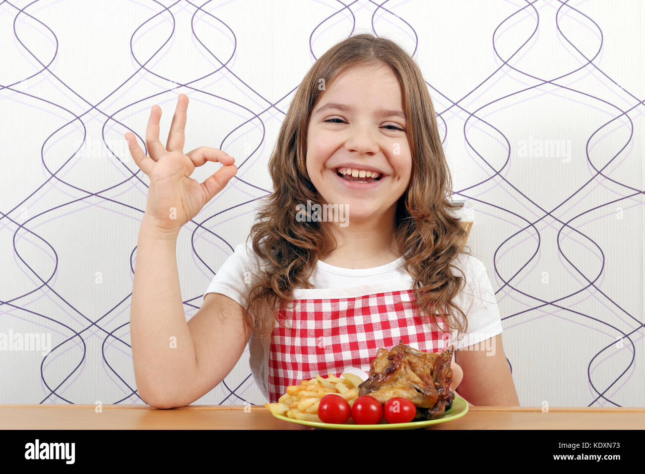 Glückliche kleine Mädchen mit gerösteten Chicken Wings und ok Handzeichen Stockfoto