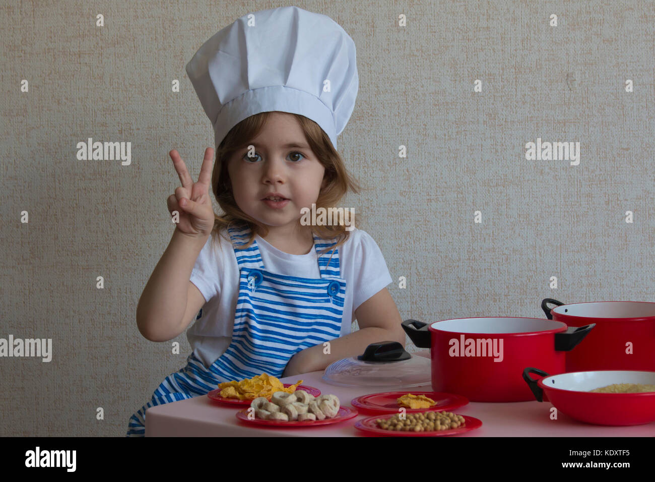 Portrait adorable kleine Mädchen in Chef hat Kochen. zeigt Finger ein Sieg Stockfoto
