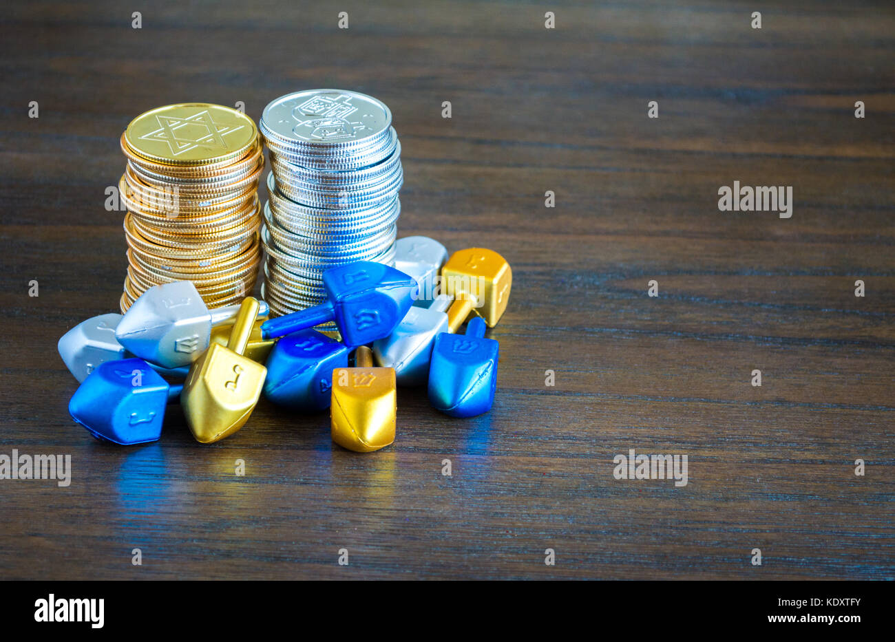 2 Stapel von Gold und Silber hanukkah Münzen umgeben von winzigen dreidels auf einem Holztisch mit Kopie Raum Stockfoto