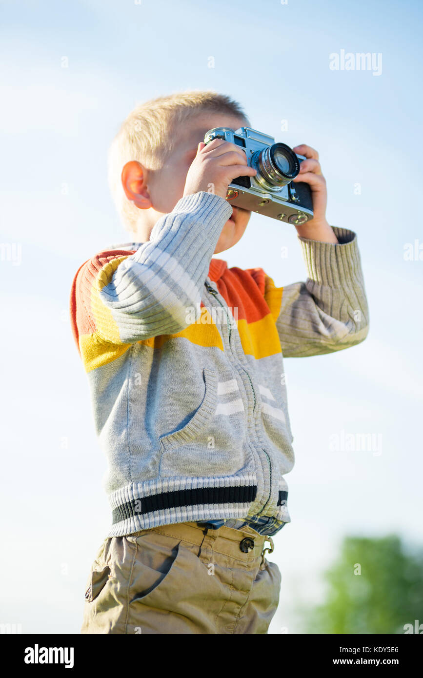 Kleiner Junge mit einer alten Kamera schießen im Freien. Stockfoto