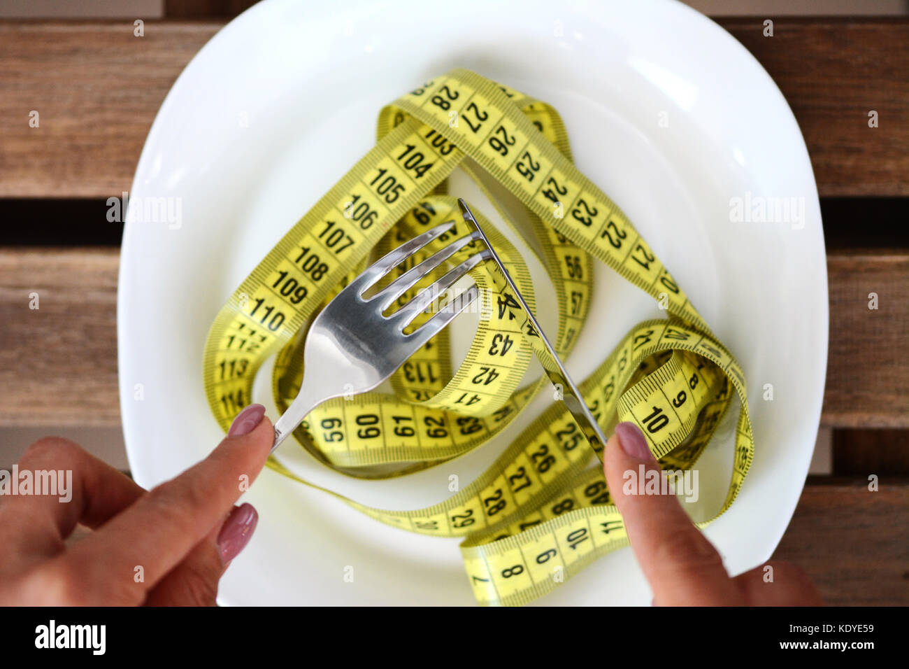 Diät Konzept mit Frau mit Messer und Gabel bereit, eine Messung Klebeband von weissen Teller zu essen, Gewicht zu verlieren für das Erhalten des Sitzes Stockfoto