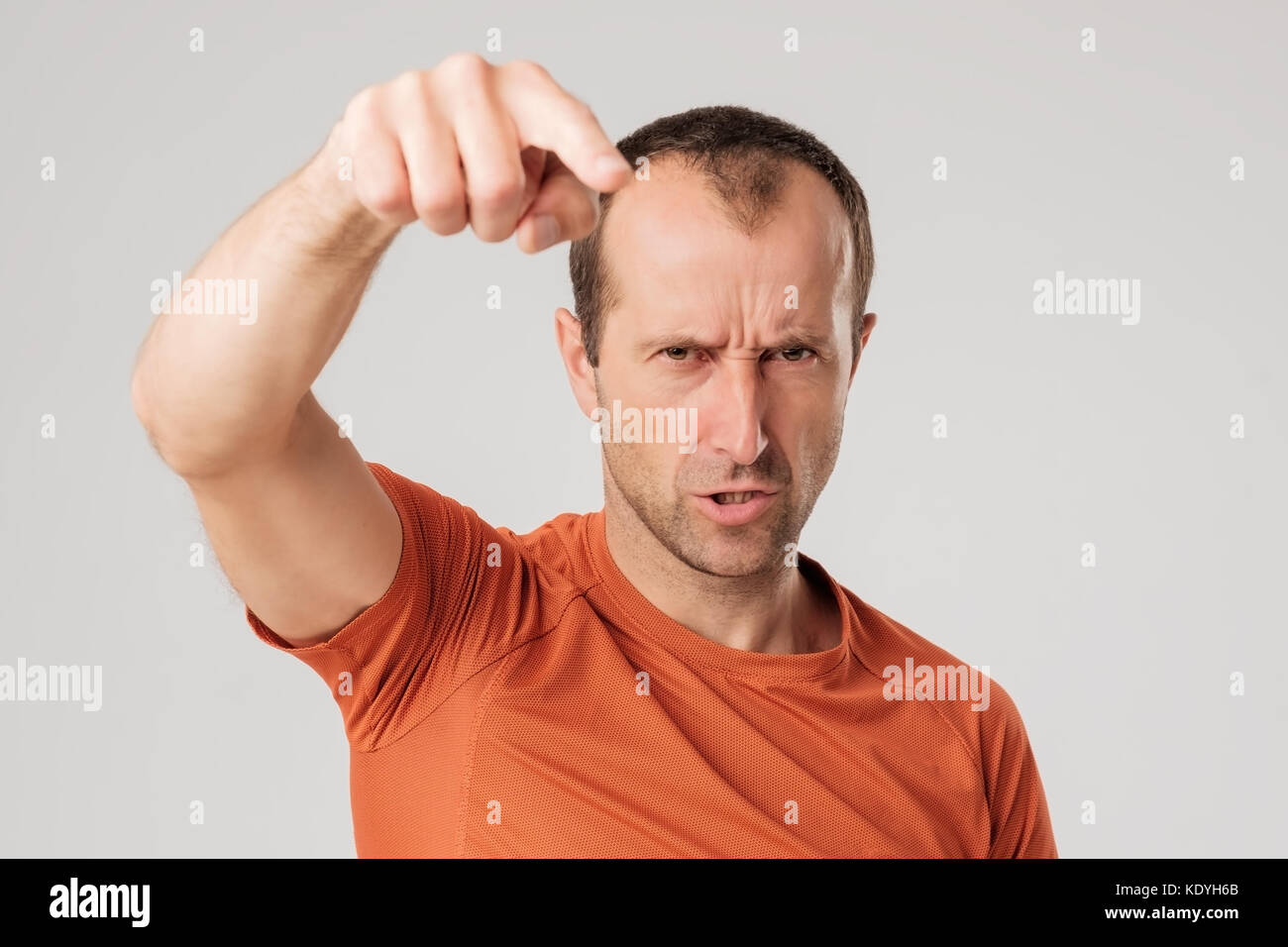 Mture Mann in orange T-shirtfinger in Richtung der Kamera auf grauem Hintergrund Stockfoto