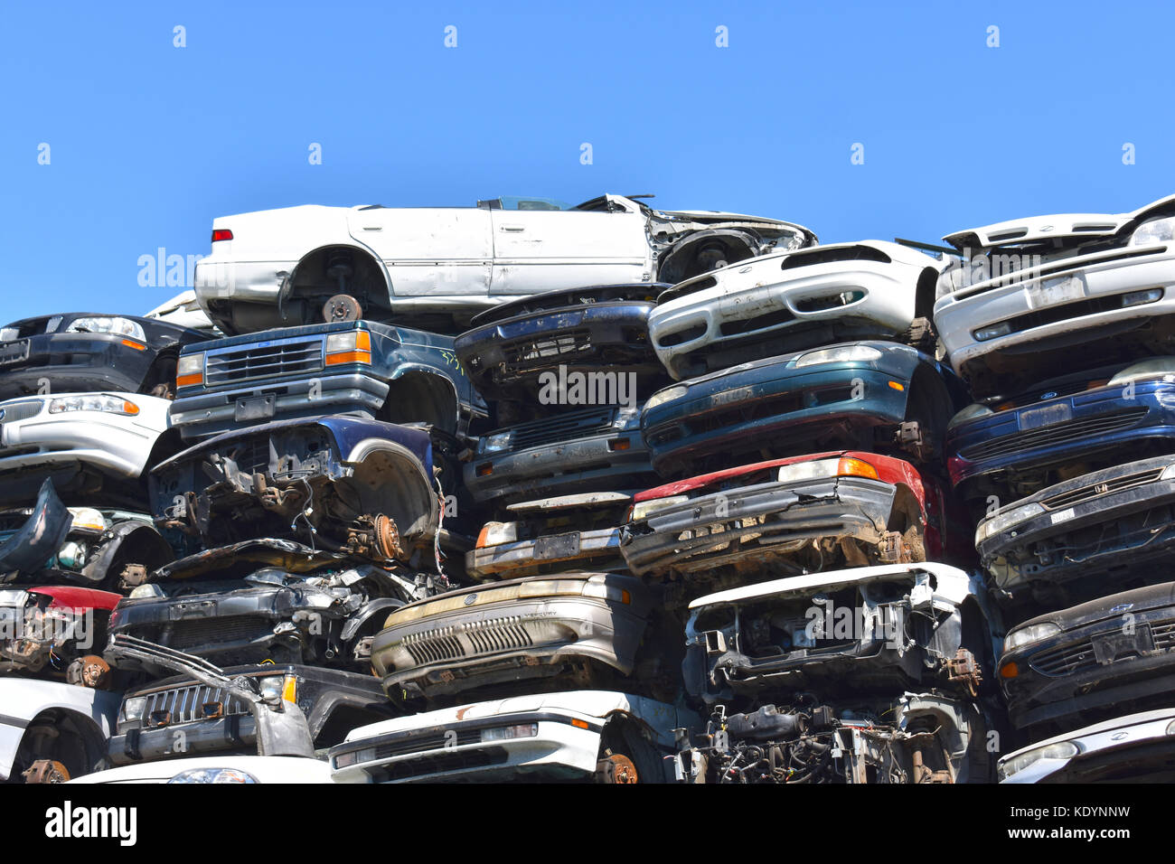 Autos stapelten sich hoch auf einem Schrottplatz mit vielen Autos, die zerquetscht und beschädigt wurden. Stockfoto