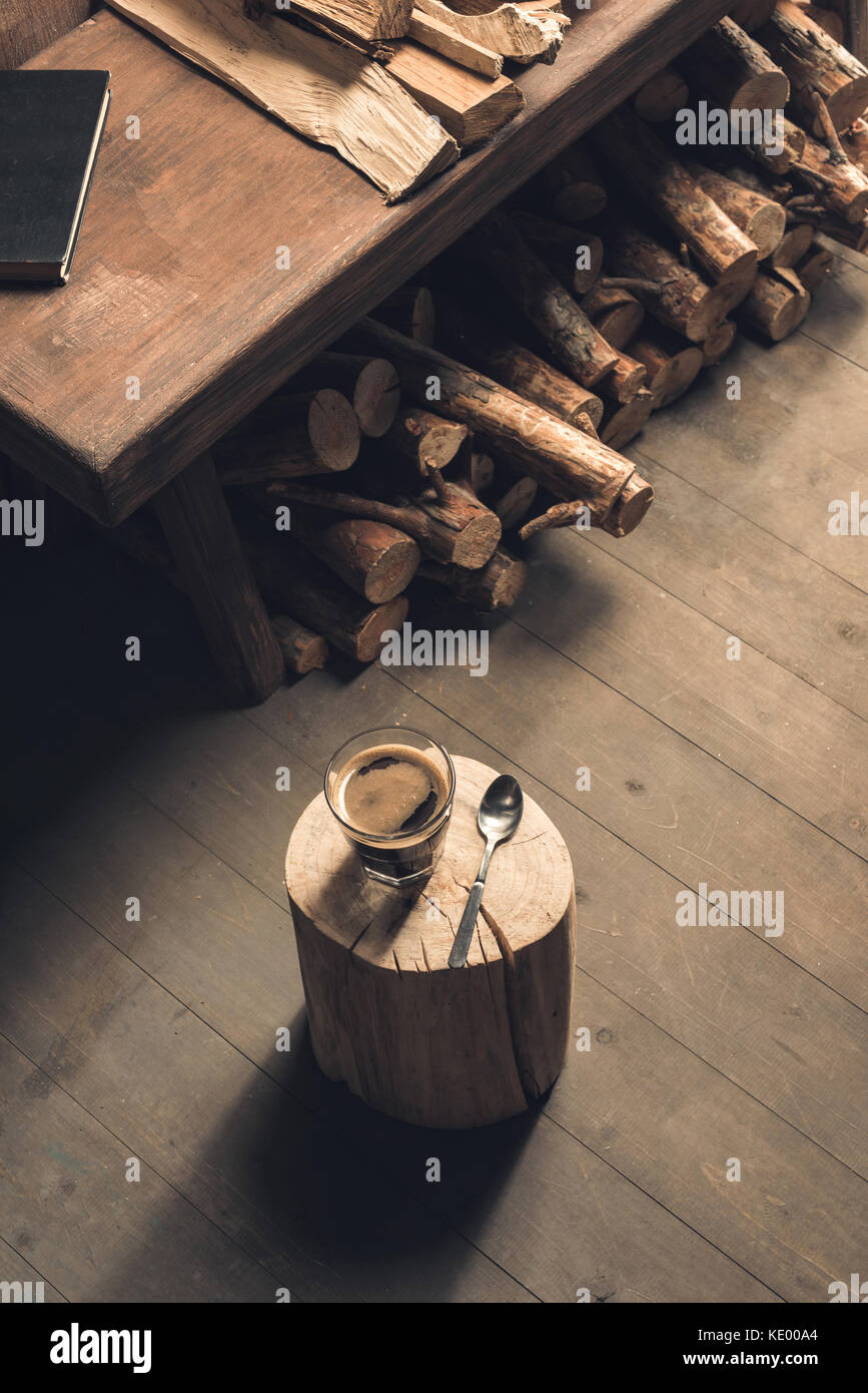 Glas Kaffee trinken und Löffel auf Holz auf dem Boden in der Nähe der Tisch in der Nähe Brennholz anmelden Stockfoto