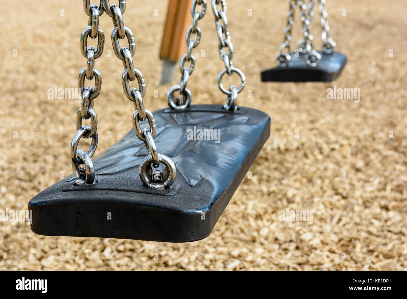 Nahaufnahme der Swing ein immer noch das Kind in schwarzem Kunststoff in einer Hackschnitzel überdachter Spielplatz mit verchromten Ketten. Stockfoto